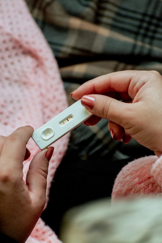 A closeup of a woman's hands with pink nails holding a positive pregnancy test